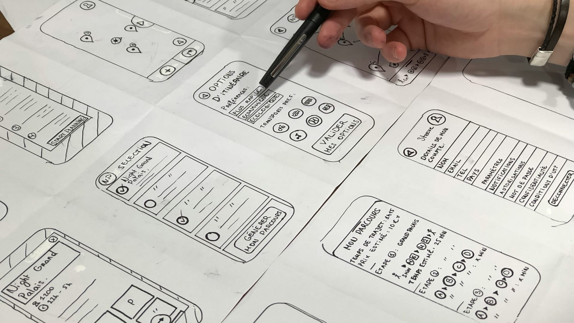 una mano disegna wireframe e schermate su fogli di carta